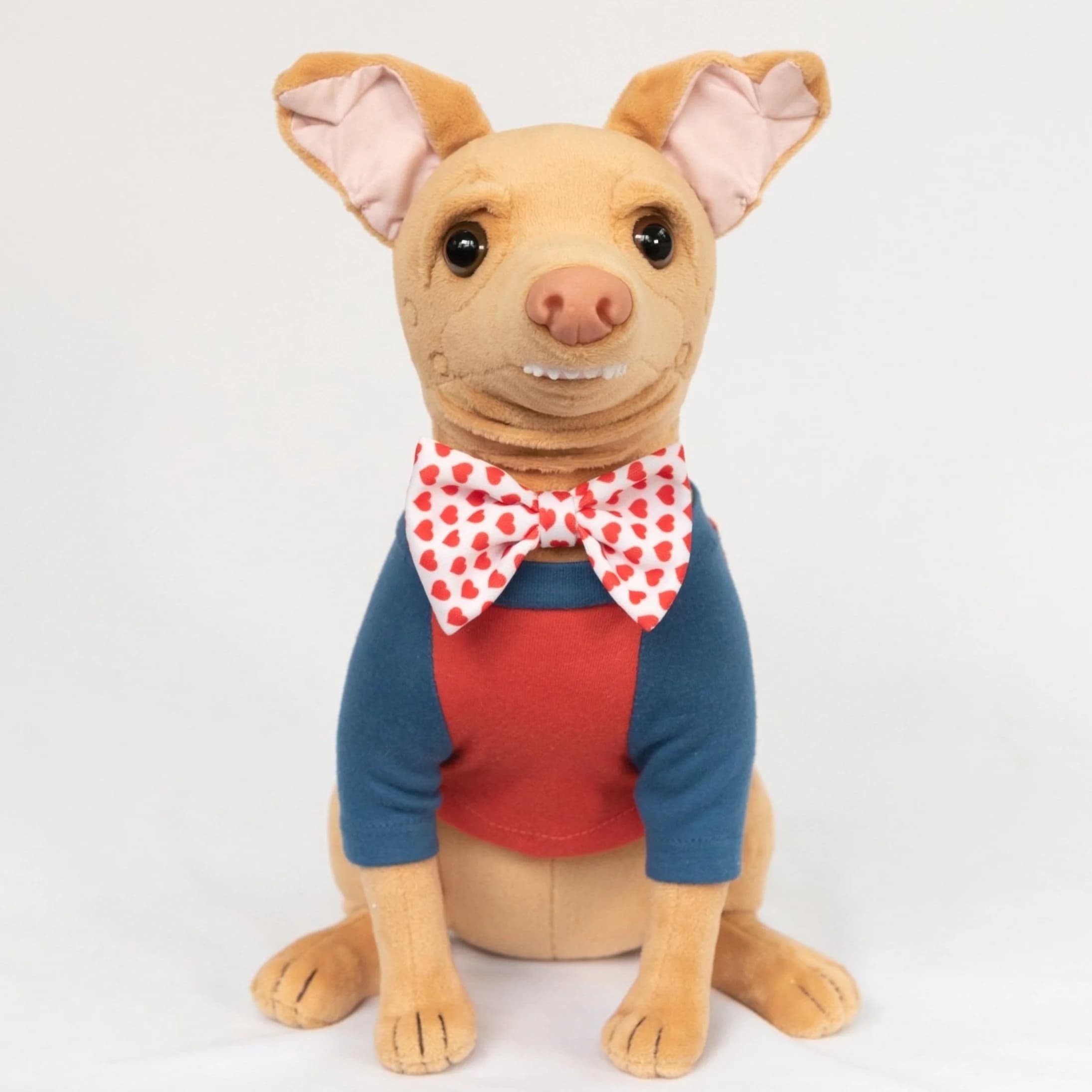 A Perfectly Imperfect Tuna plush with a slightly skewed face and crooked smile, in blue cardigan with red inner shirt and heart bowtie.